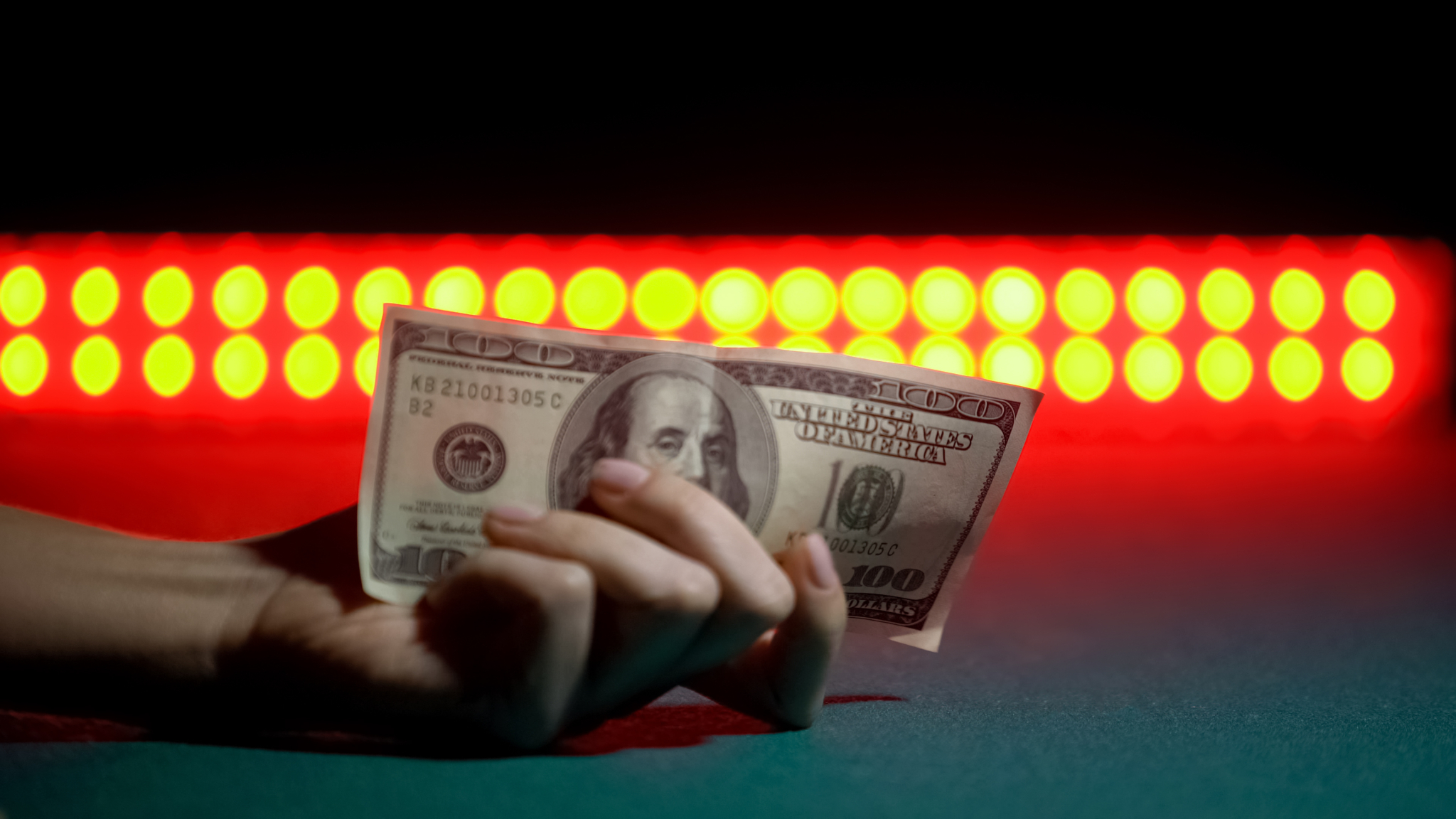 Hand holding a $100 bill under red lights, symbolizing tipping Las Vegas escorts in cash for discreet services.