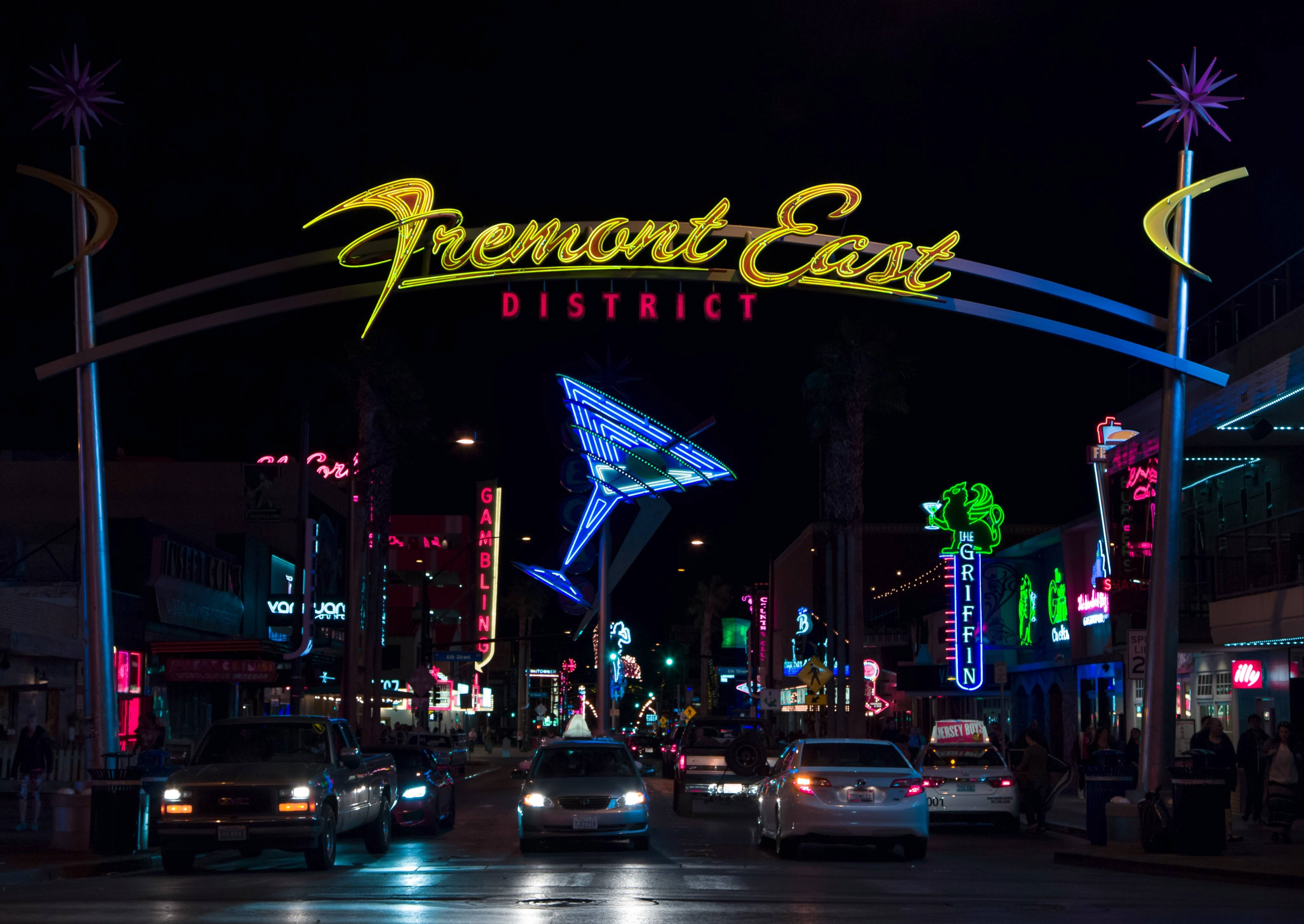 Fremont East District sign lit up at night with neon lights, cars, and bars in Downtown Las Vegas